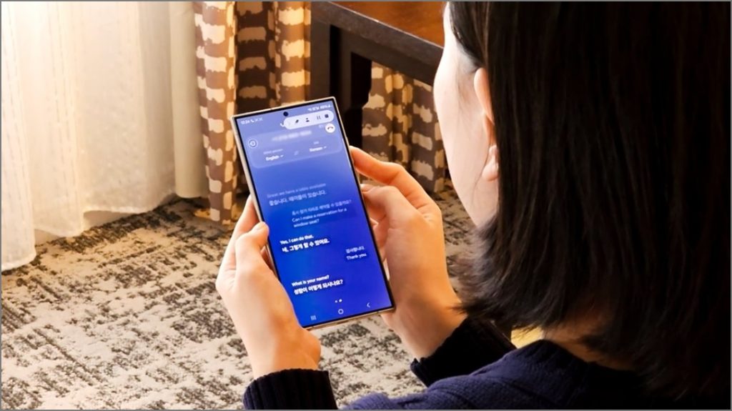 Женщина держит Samsung Galaxy S24 Ultra и демонстрирует функцию AI Live Translate для звонков.