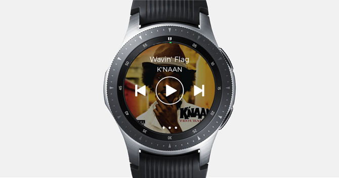 Снимок экрана Galaxy Watch с приложением Spotify, элементами управления музыкой и обложкой альбома на заднем плане.